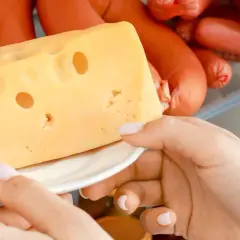 Mano che prende un pezzo di formaggio svizzero dal frigorifero, tra altri tipi di formaggio e insaccati.