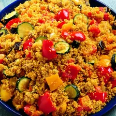 Un piatto colorato di cous cous con verdure miste: peperoni rossi e gialli, zucchine e melanzane.