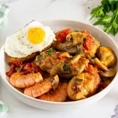 Un saporito pollo alla marengo con gamberi, funghi e pomodorini, servito con un uovo fritto su crostino.