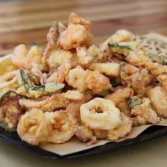 Un piatto invitante di frittura di pesce croccante, con gamberi, anelli di calamaro e verdure, accompagnato da uno spicchio di limone.