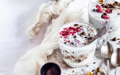 Due bicchieri di yogurt con semi di chia, lamponi e granella di nocciole. Un dessert sano e gustoso.