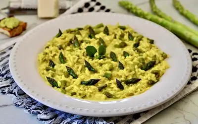 Un cremoso risotto con asparagi, guarnito con punte di asparagi freschi e una fogliolina verde.