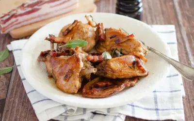 Delizioso coniglio in padella, dorato e succulento, guarnito con pancetta croccante e foglie di salvia fresca.