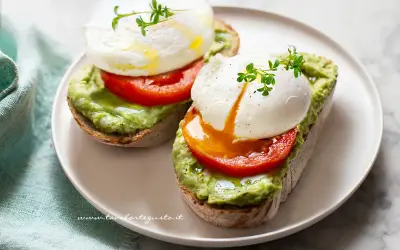 Due fette di pane tostato con avocado, pomodoro e un perfetto uovo in camicia, guarnito con germogli freschi.