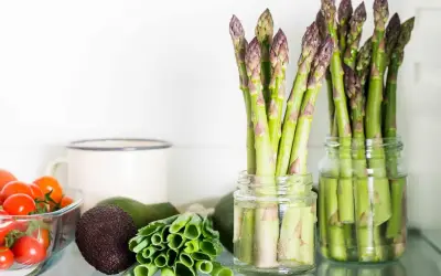 Asparagi freschi in barattoli con acqua, un ottimo modo per conservare gli asparagi. Vicino pomodorini, avocado e cipollotti.
