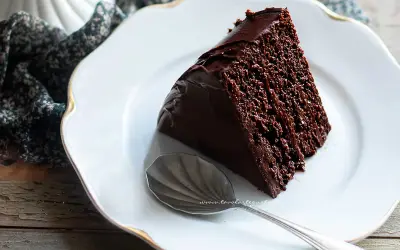Una fetta di torta al cioccolato, ricca e umida, su un piatto bianco con un cucchiaino.