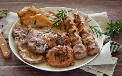 Un piatto ricco di **grigliata di carne**: costine, spiedini, salsicce e hamburger, guarniti con rosmarino fresco.