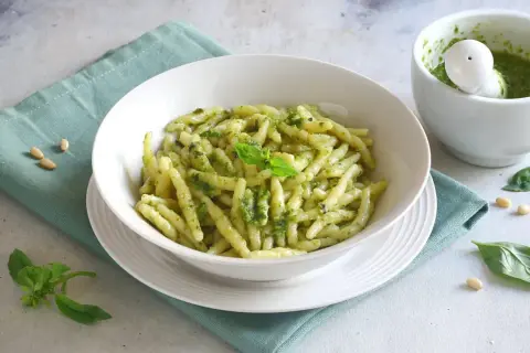 Un piatto invitante di pasta al pesto, condita con basilico fresco e pinoli. Accanto, un mortaio con altro pesto fatto in casa.