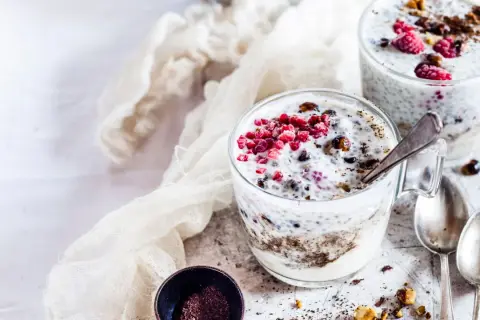 Due bicchieri di yogurt con semi di chia, lamponi e granella di nocciole. Un dessert sano e gustoso.