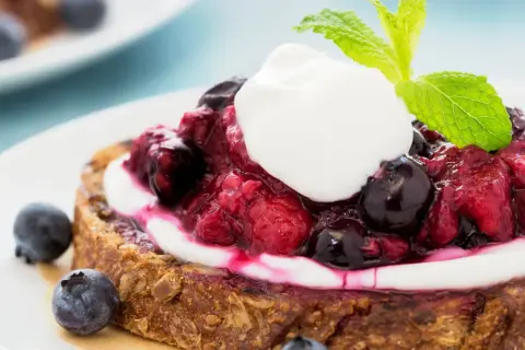 Fetta di pane integrale con yogurt greco, frutti di bosco e menta. Una deliziosa colazione con yogurt greco.