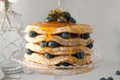 Pancake senza latte, una torre dorata con mirtilli freschi e sciroppo d'acero che cola.