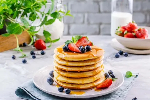 Pila di soffici pancake senza glutine, guarniti con fragole, mirtilli e sciroppo d'acero.
