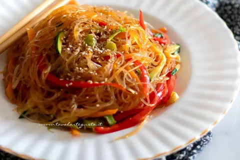 Un piatto invitante di spaghetti di soia con verdure colorate, peperoni rossi, zucchine e carote, guarnito con semi di sesamo.
