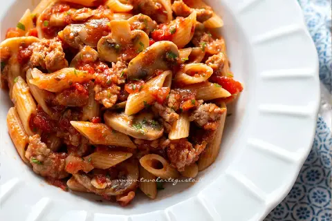 Piatto di pasta alla boscaiola con penne, funghi, salsiccia e pomodoro, condita con prezzemolo fresco.