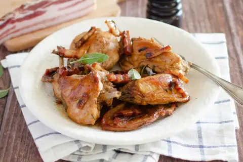 Delizioso coniglio in padella, dorato e succulento, guarnito con pancetta croccante e foglie di salvia fresca.