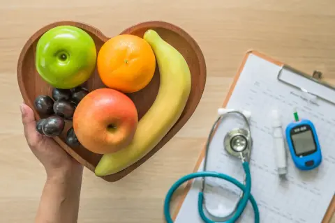Frutta fresca in un vassoio a forma di cuore, accanto a uno stetoscopio e un glucometro, per capire come abbassare la glicemia con una dieta sana.