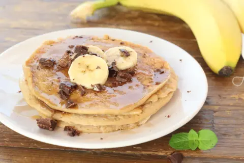 Pancake alla banana con scaglie di cioccolato e sciroppo d'acero, guarniti con fettine di banana fresca.