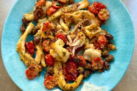 Calamari gratinati al forno con pomodorini e olive, un piatto saporito e croccante servito su un piatto blu.