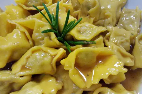 Un piatto invitante di ravioli del plin, conditi con un sugo dorato e guarniti con un rametto di rosmarino fresco.