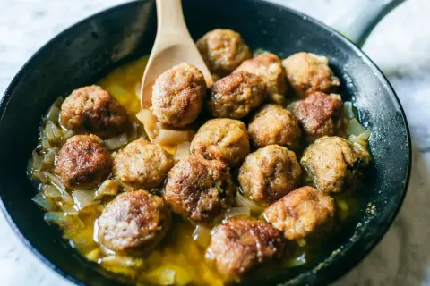 Polpette in bianco succulente in padella con cipolle caramellate, pronte per essere gustate.