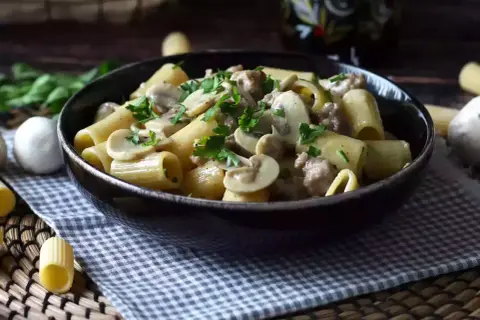 Piatto fumante di pasta con funghi e salsiccia, guarnito con prezzemolo fresco. Un classico confortante.