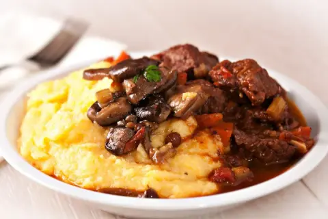 Polenta cremosa con spezzatino di manzo e funghi. Un classico piatto italiano, perfetto per scoprire polenta con cosa accompagnarla.