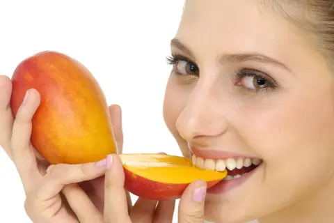 Ragazza sorridente morde un mango succoso, sapendo che il mango è lassativo.