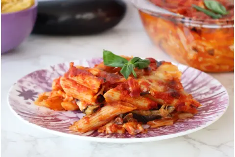 Piatto di pasta alla siciliana con melanzane, pomodoro e formaggio fuso, guarnito con basilico fresco.