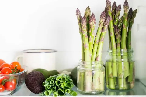 Asparagi freschi in barattoli con acqua, un ottimo modo per conservare gli asparagi. Vicino pomodorini, avocado e cipollotti.