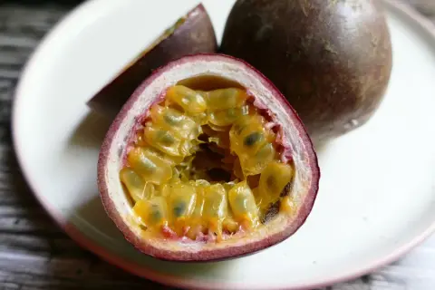 Un frutto della passione tagliato a metà, con la polpa succosa e i semi visibili, su un piatto bianco.