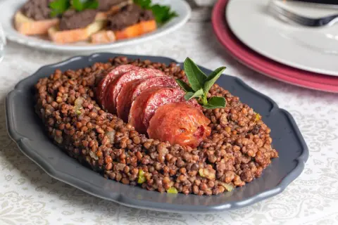 Piatto di lenticchie con fette di cotechino fresco, guarnito con una fogliolina di salvia.