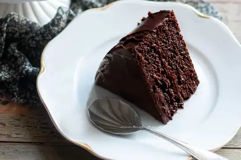 Una fetta di torta al cioccolato, ricca e umida, su un piatto bianco con un cucchiaino.