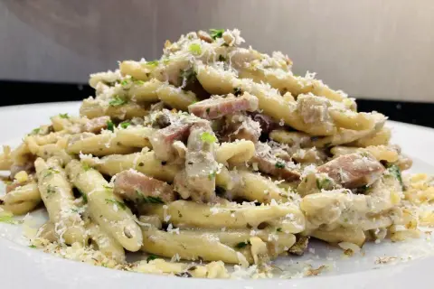 Un piatto invitante di pasta con speck, condita con una cremosa salsa, prezzemolo tritato e abbondante parmigiano grattugiato.