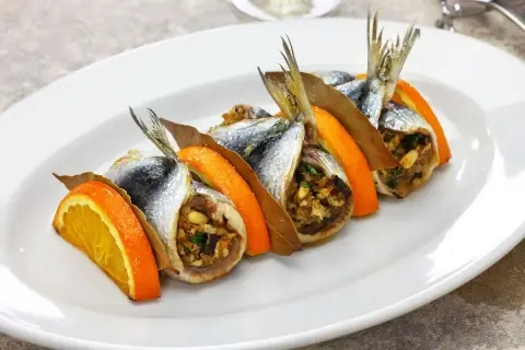 Sarde a beccafico su un piatto bianco, guarnite con fette d'arancia e foglie di alloro. Un piatto tradizionale siciliano.
