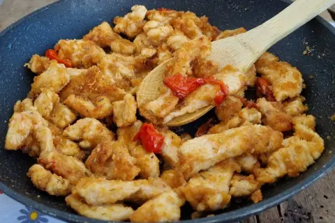 Straccetti di pollo dorati e saporiti in padella con pomodorini, pronti per essere gustati.