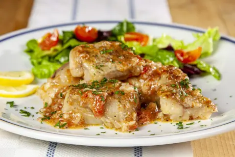 Deliziosi bocconcini di coda di rospo in umido con pomodoro e prezzemolo, accompagnati da insalata fresca e spicchi di limone.