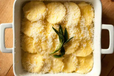 Gnocchi alla Romana pronti per essere infornati, conditi con parmigiano grattugiato e un rametto di salvia.