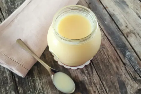 Un vasetto di latte condensato fatto in casa, denso e cremoso, pronto per dolci deliziosi. Un cucchiaino ne mostra la consistenza perfetta.