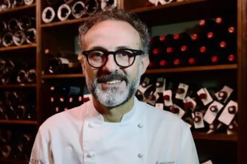 Un sorriso tra gli scaffali di bottiglie di vino, un ritratto di uno dei tanti chef stellati italiani che rendono la cucina italiana famosa nel mondo.