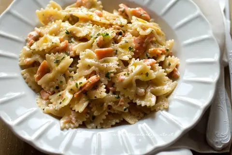 Farfalle cremose con pezzetti di salmone e prezzemolo tritato, un piatto invitante di pasta al salmone.
