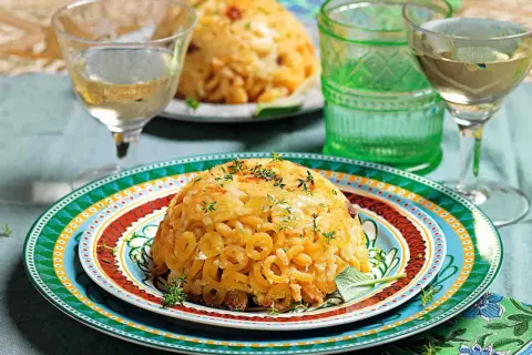 Anelletti al forno dorati e invitanti, guarniti con erbe aromatiche, serviti su piatti colorati con bicchieri di vino bianco.