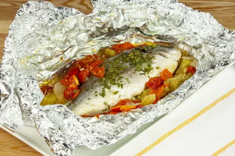 Orata al cartoccio con pomodorini e verdure, cotta al forno in un involucro di alluminio, pronta per essere gustata.