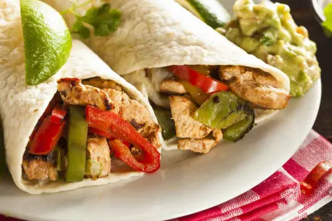 Due fajitas di pollo con peperoni, cipolle e guacamole. Un piatto saporito e colorato, pronto per essere gustato.