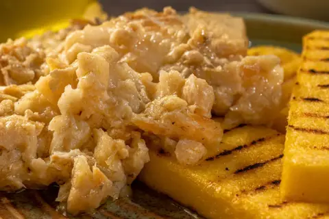 Un saporito baccalà alla vicentina, cremoso e profumato, servito su fette di polenta grigliata.