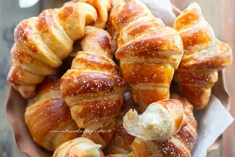 Cornetti fatti in casa dorati e soffici, spolverati di zucchero a velo, invitano a una colazione golosa.