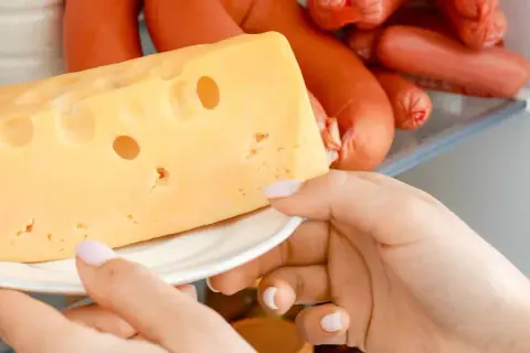 Mano che prende un pezzo di formaggio svizzero dal frigorifero, tra altri tipi di formaggio e insaccati.