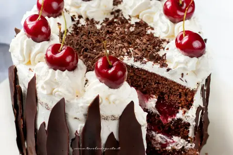 Una fetta di foresta nera torta, con panna montata, ciliegie fresche e riccioli di cioccolato.