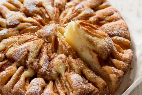Una deliziosa torta di mele, cosparsa di zucchero a velo, con una fetta rimossa che rivela la morbida consistenza.