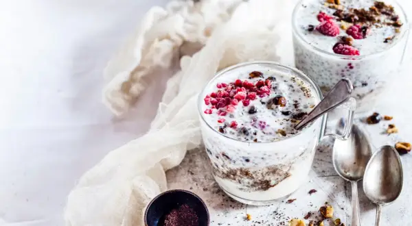 Due bicchieri di yogurt con semi di chia, lamponi e granella di nocciole. Un dessert sano e gustoso.