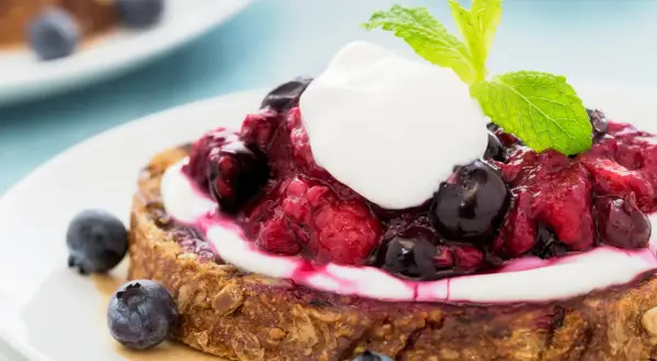 Fetta di pane integrale con yogurt greco, frutti di bosco e menta. Una deliziosa colazione con yogurt greco.